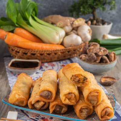 Involtini primavera dorati e croccanti impilati su un piatto con salsa di soia e verdure fresche sullo sfondo