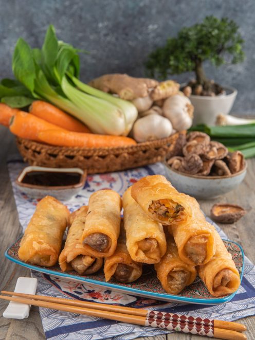 Involtini primavera dorati e croccanti impilati su un piatto con salsa di soia e verdure fresche sullo sfondo