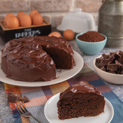 Mud cake al cioccolato con glassa lucida, fetta servita accanto alla torta tagliata