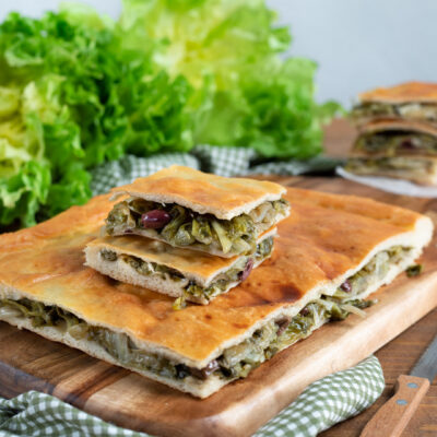 Pizza di scarola farcita con scarola brasata e olive, tagliata a fette su tagliere