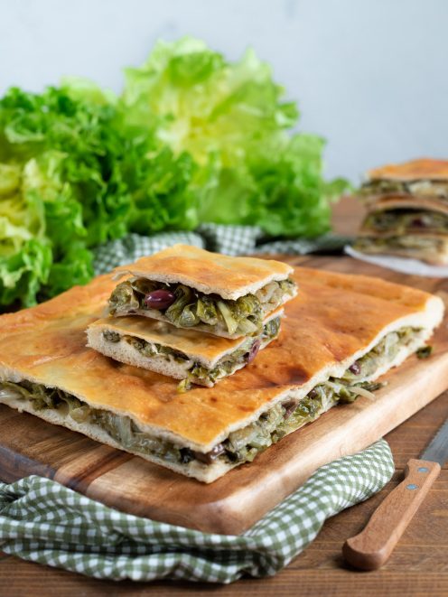 Pizza di scarola farcita con scarola brasata e olive, tagliata a fette su tagliere