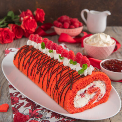 Rotolo red velvet farcito con panna e lamponi, decorato con cioccolato fondente e foglioline di menta
