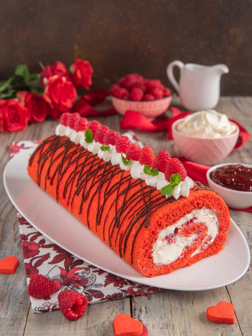 Rotolo red velvet farcito con panna e lamponi, decorato con cioccolato fondente e foglioline di menta