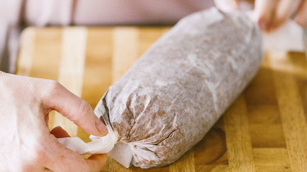 Rotolo di salame di cioccolato avvolto nella carta forno, le mani ne chiudono le estremità
