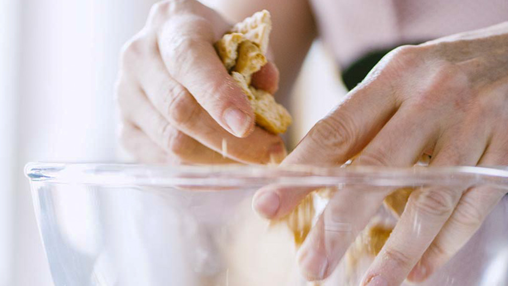 Mani che sbriciolano grossolanamente dei biscotti secchi in una ciotola