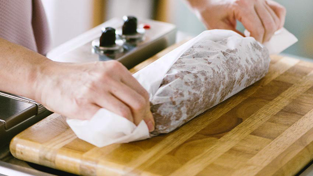Mani che avvolgono il salame di cioccolato in carta forno formando un cilindro compatto