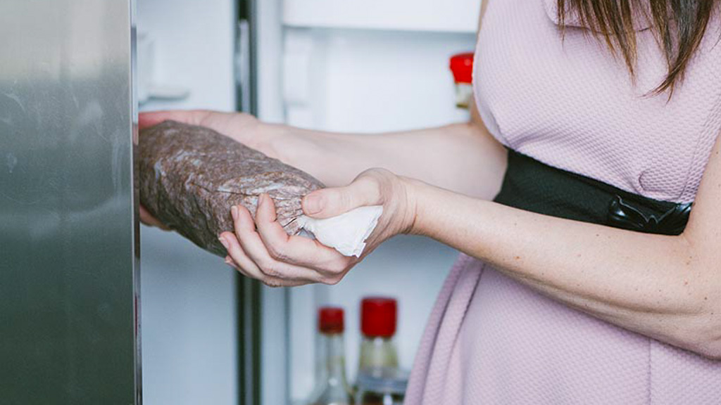 Mani che estraggono il salame di cioccolato dal frigorifero avvolto nella carta