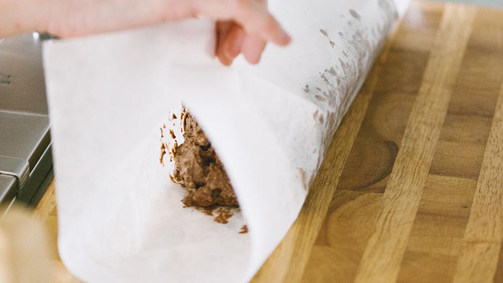 Mano che avvolge il composto per salame di cioccolato nella carta forno formando un cilindro