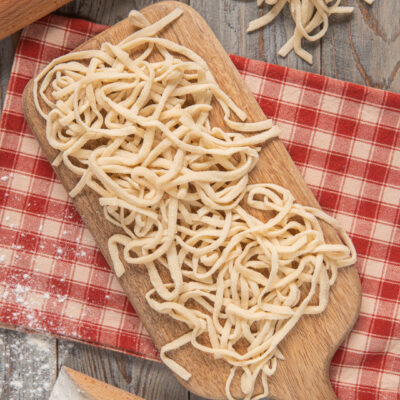 Tonnarelli freschi appena tagliati su tagliere, con farina e mattarello sullo sfondo