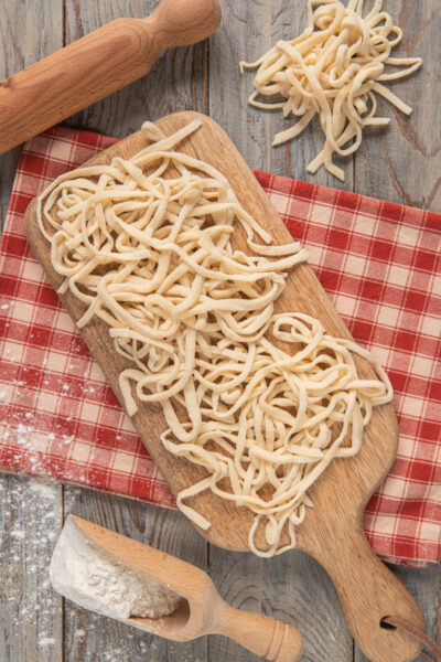 Tonnarelli freschi appena tagliati su tagliere, con farina e mattarello sullo sfondo