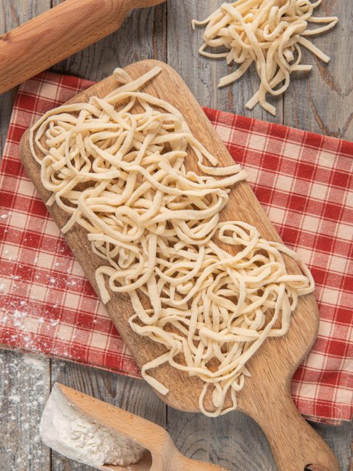Tonnarelli freschi appena tagliati su tagliere, con farina e mattarello sullo sfondo