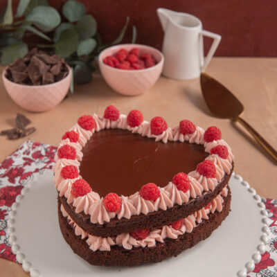 Torta cuore al cioccolato con ganache lucida, ciuffi di crema ai lamponi e lamponi freschi