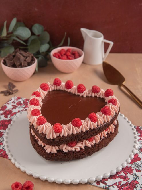 Torta cuore al cioccolato con ganache lucida, ciuffi di crema ai lamponi e lamponi freschi