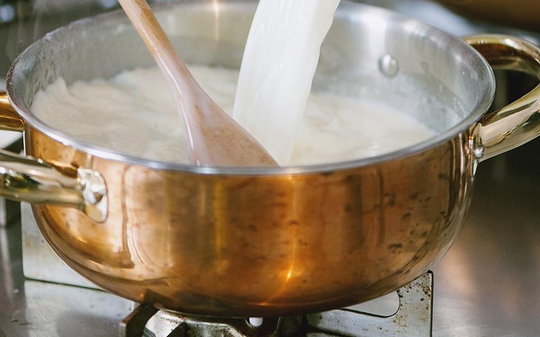 Latte versato a filo nella besciamella mentre si mescola con un cucchiaio di legno