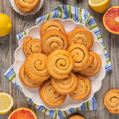 Arancini e limoncini di carnevale a spirale disposti su piatto circondato da agrumi tagliati