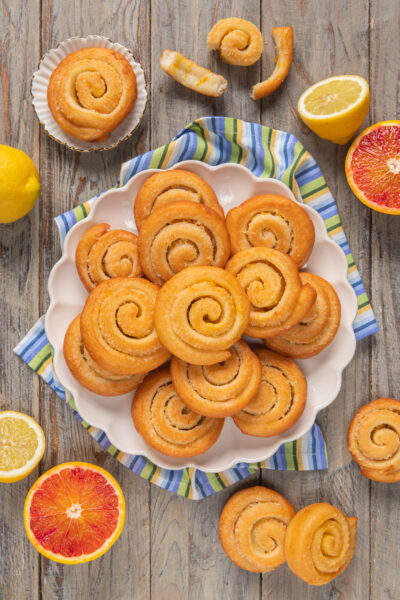 Arancini e limoncini di carnevale a spirale disposti su piatto circondato da agrumi tagliati