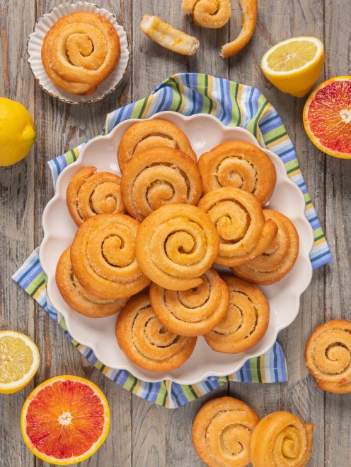 Arancini e limoncini di carnevale a spirale disposti su piatto circondato da agrumi tagliati
