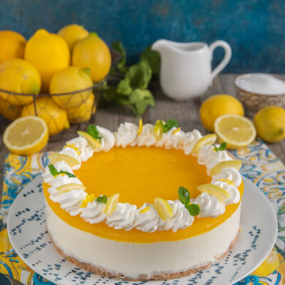 Cheesecake al limone con gelatina gialla, ciuffi di panna e fettine di limone fresco