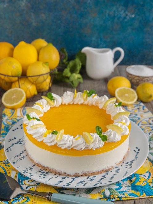 Cheesecake al limone con gelatina gialla, ciuffi di panna e fettine di limone fresco