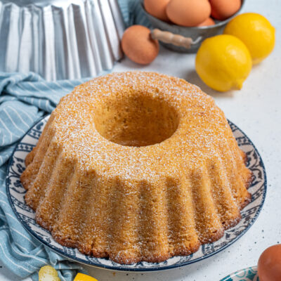 Ciambellone dorato spolverato di zucchero a velo, con scorze di limone accanto