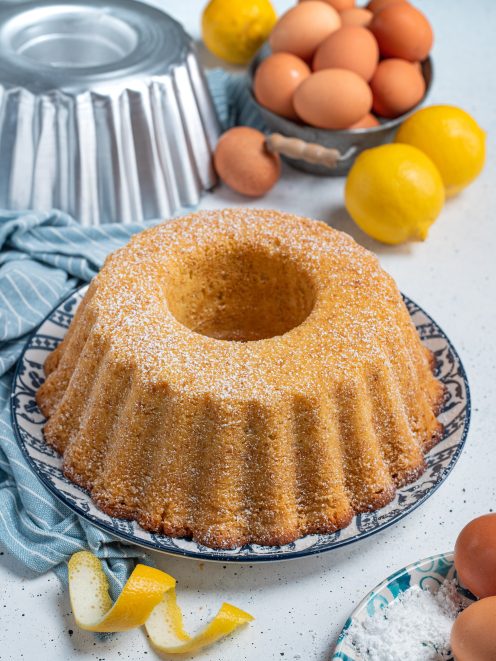 Ciambellone dorato spolverato di zucchero a velo, con scorze di limone accanto