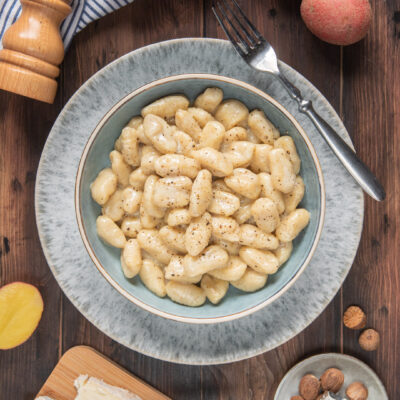 Gnocchi al gorgonzola conditi con pepe nero, serviti in una ciotola con formaggio e noci moscate accanto