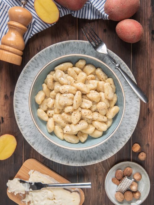 Gnocchi al gorgonzola conditi con pepe nero, serviti in una ciotola con formaggio e noci moscate accanto