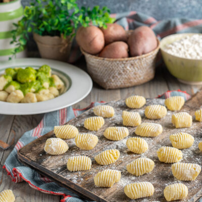 Gnocchi di patate freschi rigati su tagliere infarinato, con patate rosse e farina sullo sfondo
