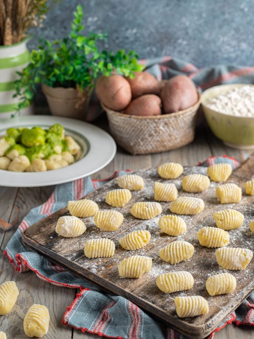Gnocchi di patate freschi rigati su tagliere infarinato, con patate rosse e farina sullo sfondo