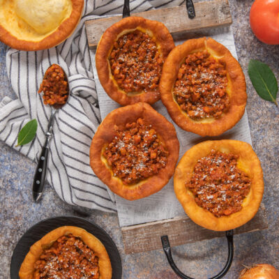 Kniekiechl salati farciti con ragù di carne e spolverata di parmigiano su tagliere di legno