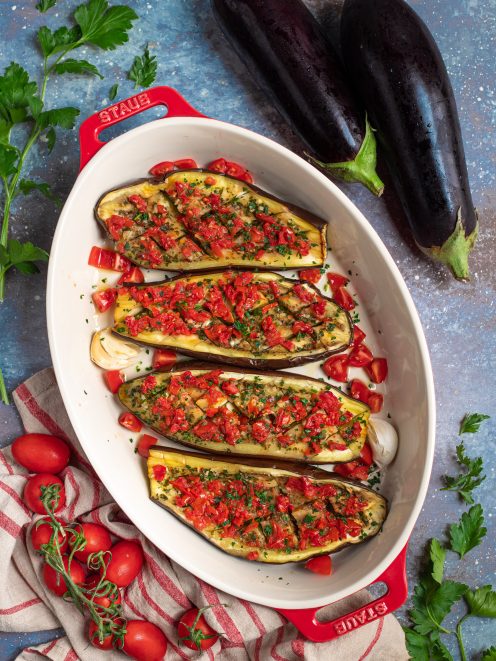 Melanzane al forno tagliate a metà con pomodorini a pezzi, aglio e prezzemolo tritato