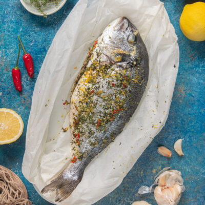 Orata al cartoccio condita con erbe aromatiche, scorza di limone e peperoncino, adagiata su carta forno