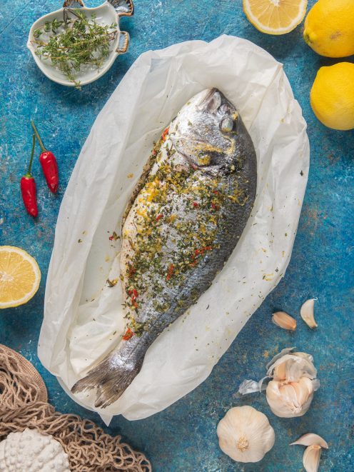 Orata al cartoccio condita con erbe aromatiche, scorza di limone e peperoncino, adagiata su carta forno