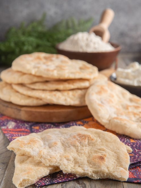 Pane naan appena cotto, uno spezzato in primo piano che mostra la mollica soffice all'interno