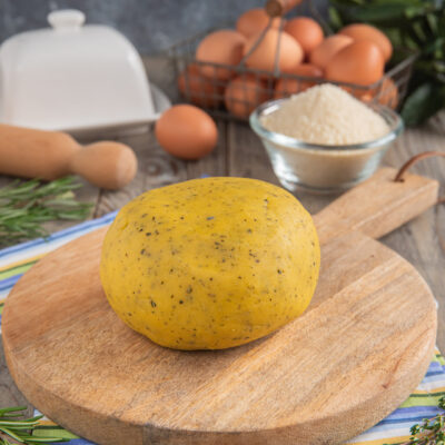 Pasta frolla salata alle erbe aromatiche pronta per essere stesa, con uova e farina sullo sfondo