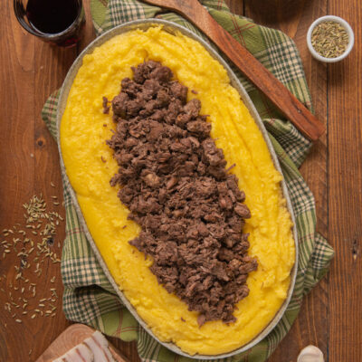 Polenta e bruscitt serviti in un vassoio ovale, con la carne sfilacciata adagiata sulla polenta morbida