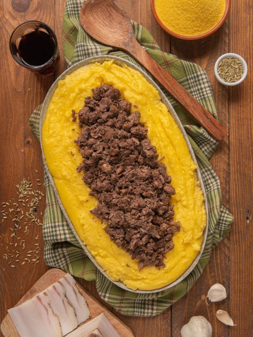 Polenta e bruscitt serviti in un vassoio ovale, con la carne sfilacciata adagiata sulla polenta morbida