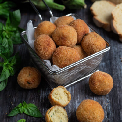 Polpette di melanzane fritte con panatura dorata, una spezzata mostra il ripieno morbido con basilico
