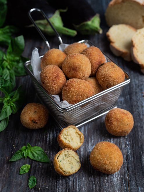 Polpette di melanzane fritte con panatura dorata, una spezzata mostra il ripieno morbido con basilico