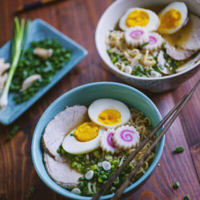 Ramen con noodles, uova sode tagliate a metà, chashu di maiale e narutomaki su brodo con erba cipollina