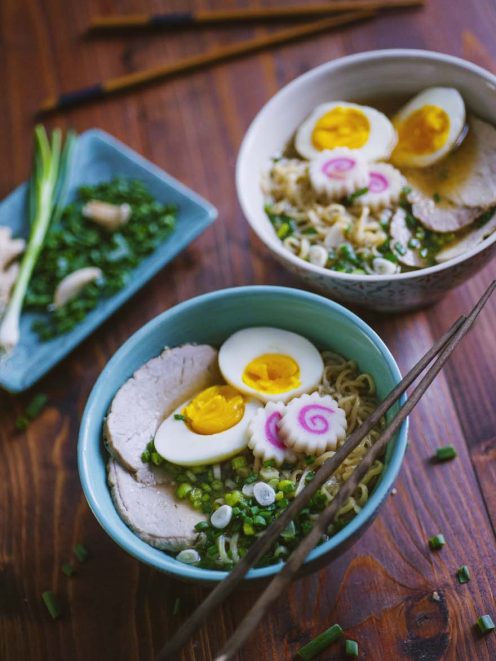 Ramen con noodles, uova sode tagliate a metà, chashu di maiale e narutomaki su brodo con erba cipollina