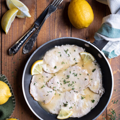 Scaloppine al limone in padella con salsa cremosa, spicchi di limone e timo fresco