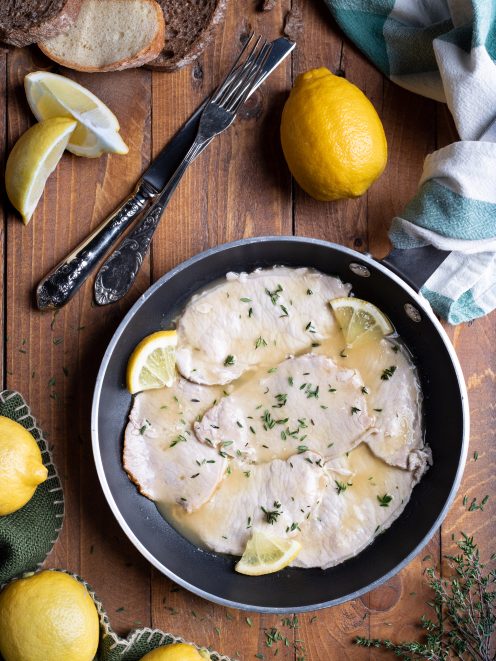 Scaloppine al limone in padella con salsa cremosa, spicchi di limone e timo fresco