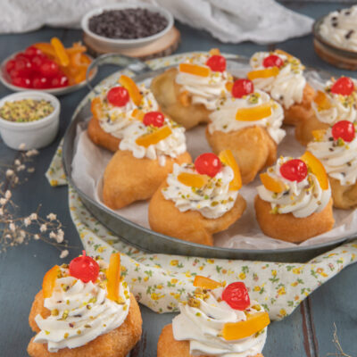 Sfinci di San Giuseppe farcite con crema, guarnite di ciliegie candite, scorza d'arancia e pistacchi tritati