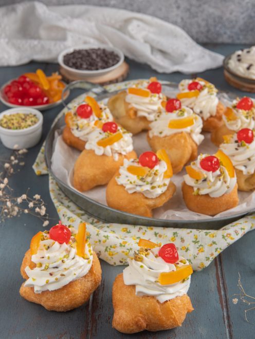 Sfinci di San Giuseppe farcite con crema, guarnite di ciliegie candite, scorza d'arancia e pistacchi tritati