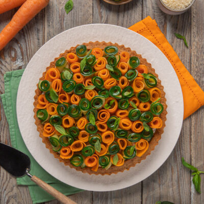 Torta salata decorata con roselline di carote e zucchine arrotolate e foglie di basilico