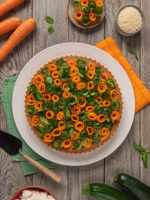 Torta salata decorata con roselline di carote e zucchine arrotolate e foglie di basilico