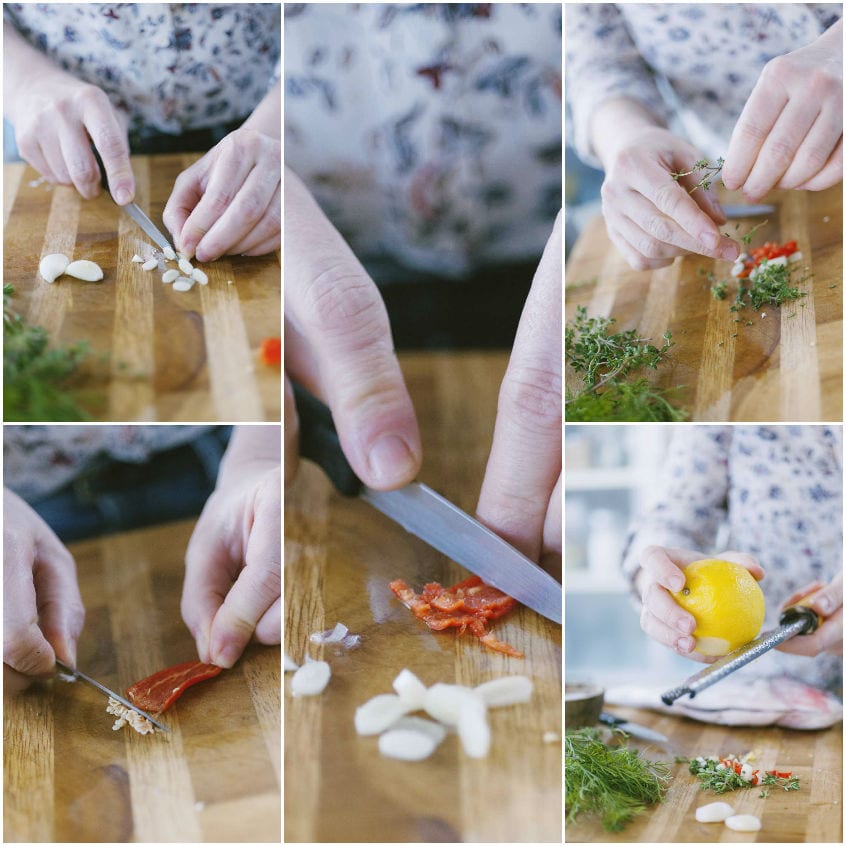 Mani che tritano aglio, peperoncino, erbe aromatiche e scorza di limone sul tagliere