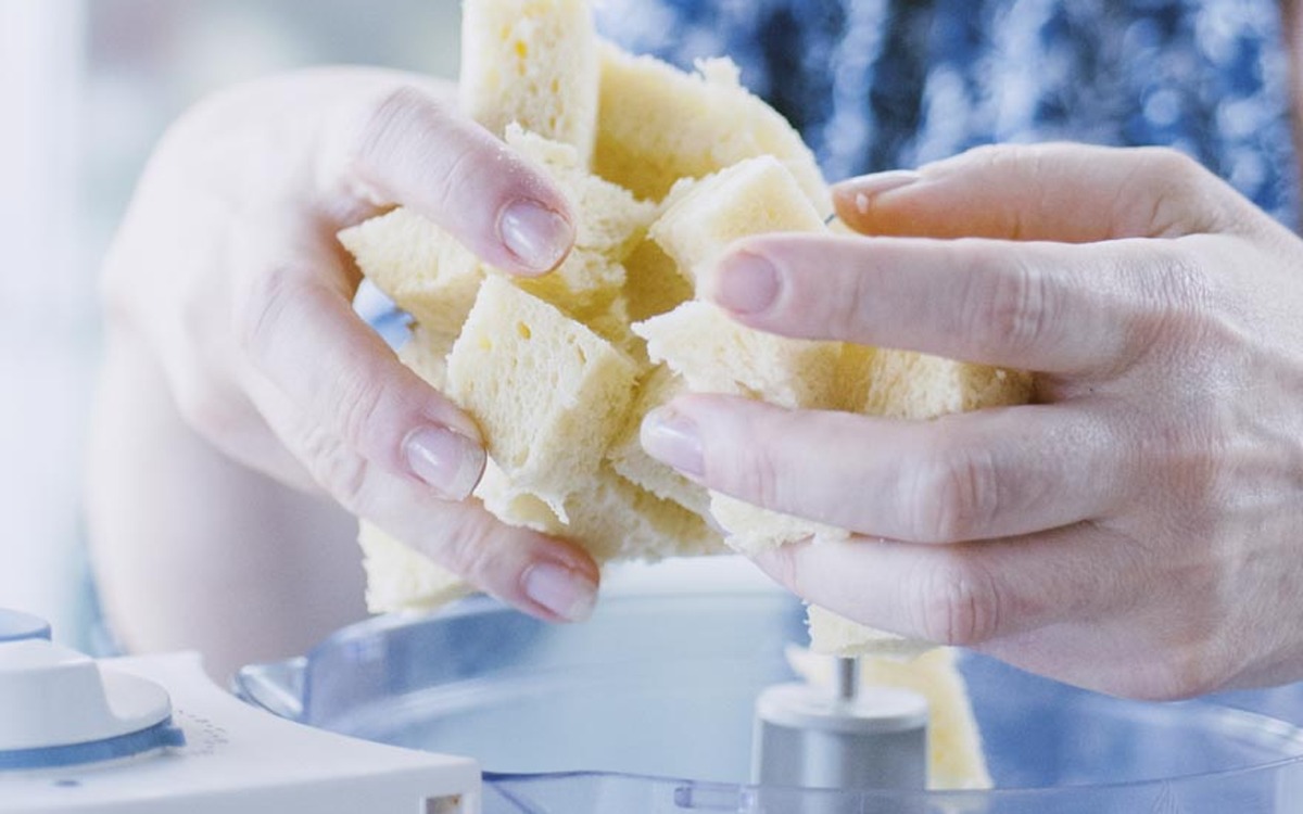 Mani che spezzano la mollica di pane raffermo a tocchetti sopra un mixer