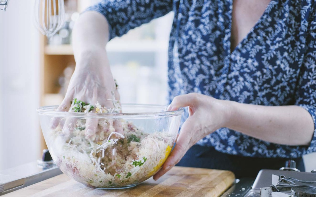 Mani che lavorano l'impasto di carne macinata con pangrattato, uovo e prezzemolo in una ciotola